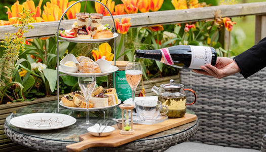 An afternoon tea set up on a table outside with orange tulips in the background and a glass of sparkling wine being poured. Alfresco Dining in Sussex. Best lunches in Brighton and Sussex