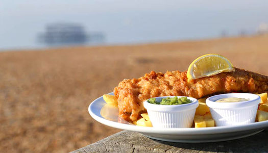 Fish and chips on Brighton beach UK - with the pier in the background on a sunny day. Picture taken at Brighton restaurant, Oh So, next to Brighton pier.
