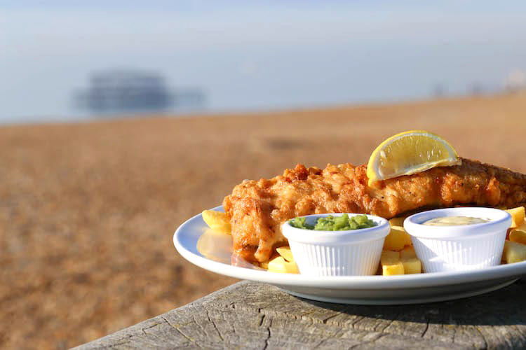 Fish and chips on the beach with the pier in the background on a sunny day. Picture taken at Brighton restaurant, Oh So, next to Brighton pier.