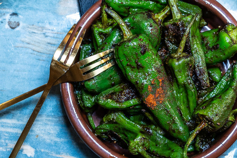 A bowl of padron peppers with two gold forks.