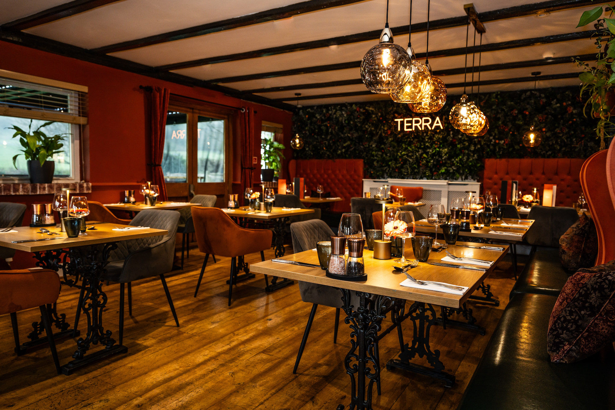 The main dining room at Tottington Manor. Low lit in a traditional setting with darkened wooden beams against a back drop of the Terra restaurant which is a brightly lit sign against a backdrop of foliage.