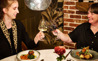 Two ladies cheersing a glass of wine in the dining room at Terra Restaurant, Tottington Manor.