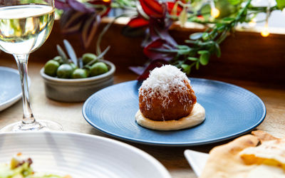 Arancini with olives and a glass of wine with plants and lights in the background.