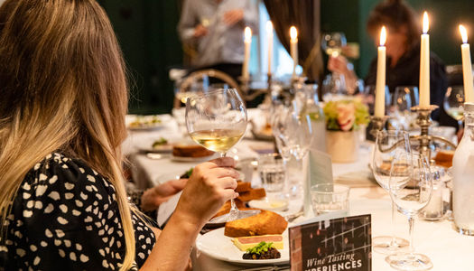 We see a large table with people sitting round taking part in a wine tasting session in Brighton. The table has food and wine and candelabras with lit candles. This is part of our Brighton wine tasting guide.