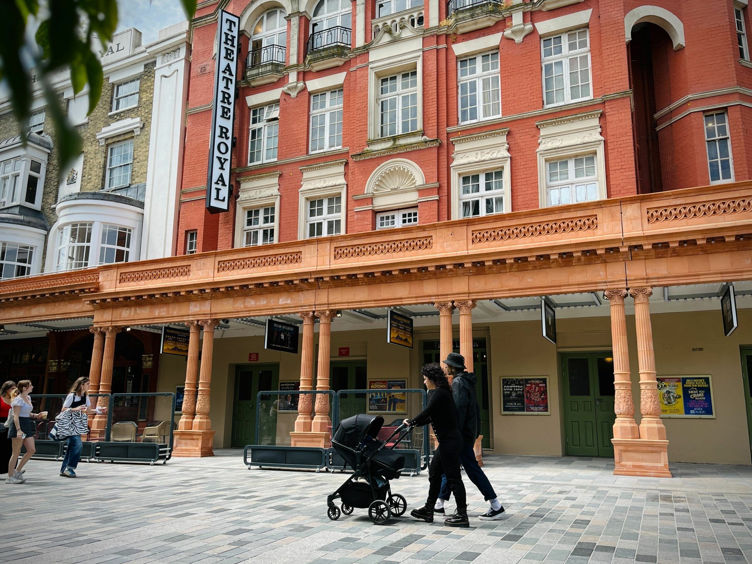 Theatre Royal exterior photo with people walking by. Red bricks and a large vertical sign.
