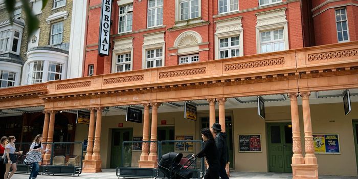 Theatre Royal exterior photo with people walking by. Red bricks and a large vertical sign.