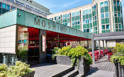 exterior of Moshimo Restaurant on a sunny day. Light green signage and red interior.