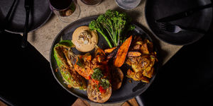 a moody photography of a vegetarian Sunday roast. Shot from above. The dish is perched on the edge of the table.