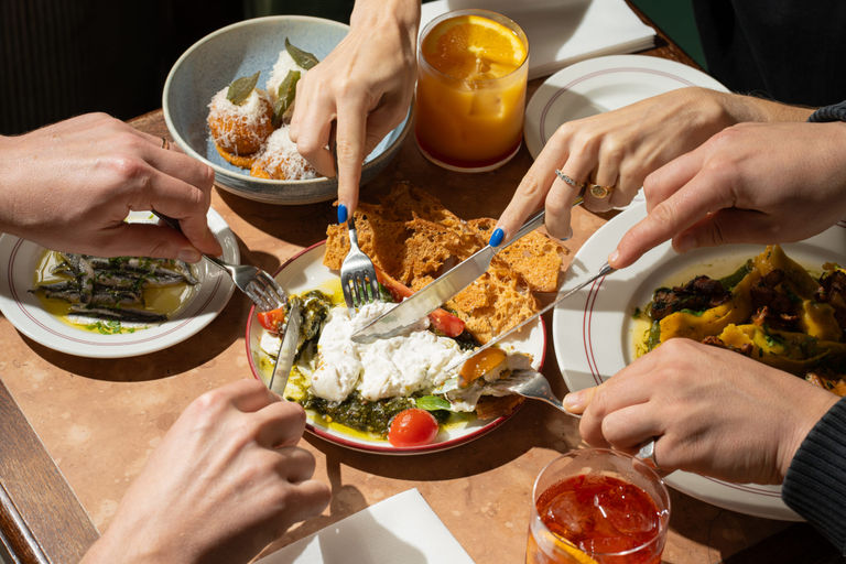 couple of people using cutlery to cut burrata on the one of sharing plates at Tutto