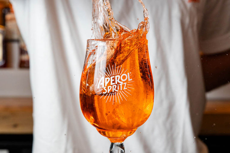 A glass of Aperol Spritz being poured with a splash of liquid.