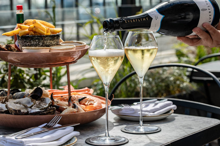 Welcome to Pearly Cow restaurant and hotel, located on Brighton's Seafront. Pictured - two glasses of bubbles being poured on the table on their seafront terrace. With seafood platter in the background