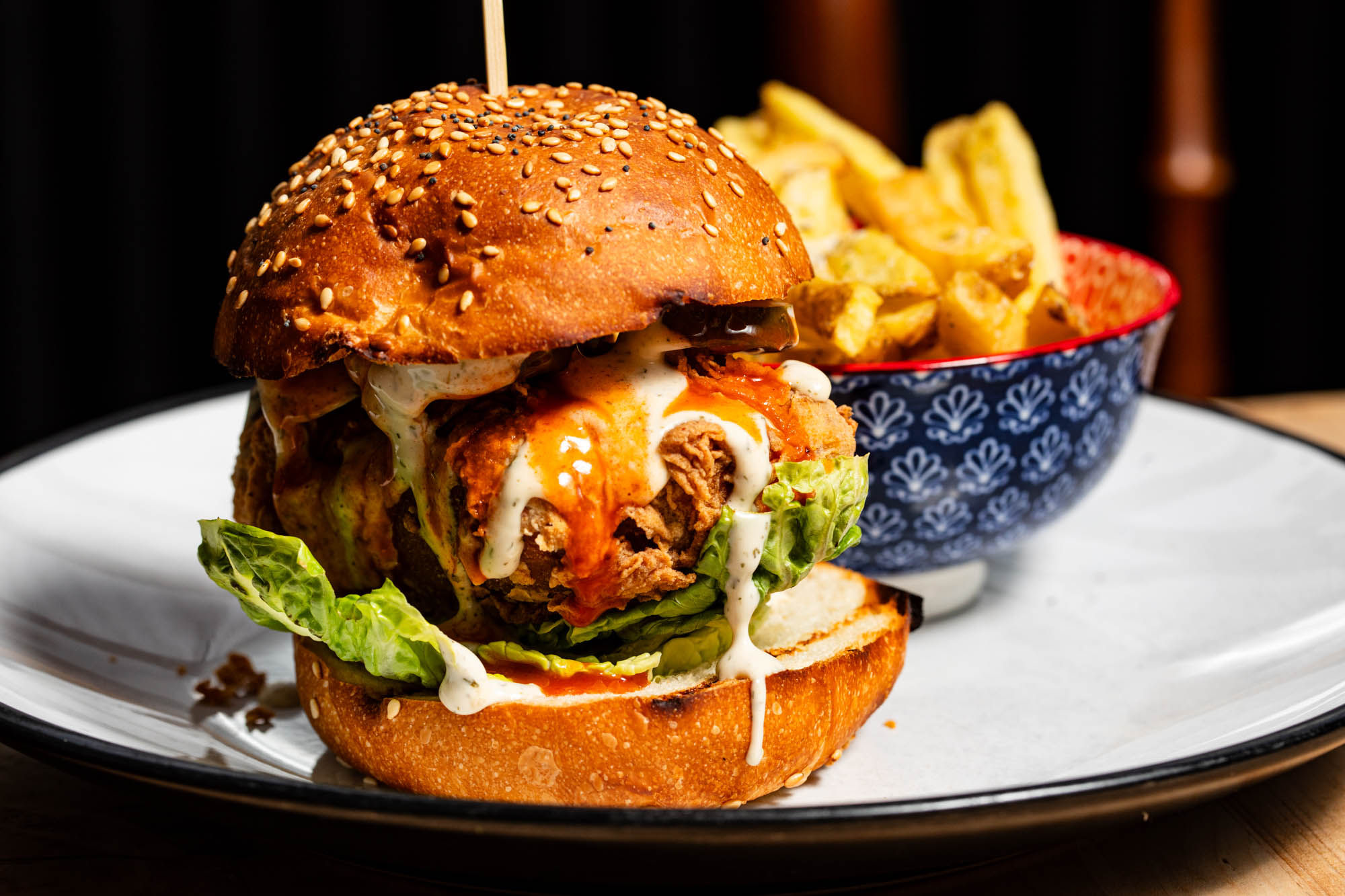 A vegan burger in a seeded bun with dripping sauce, crisp lettuce and a bowl of fries.