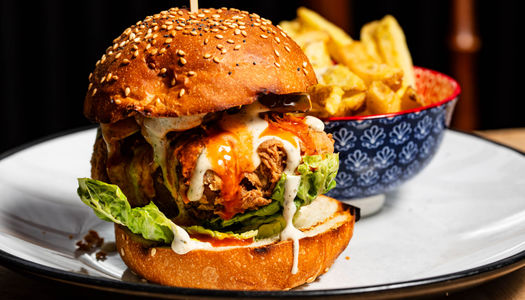 A vegan burger in a seeded bun with dripping sauce, crisp lettuce and a bowl of fries.