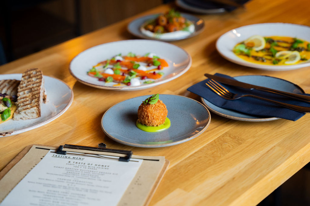 Plates of food on a wooden table with cutlery and a menu board.