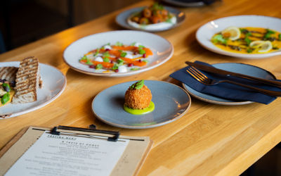 Plates of food on a wooden table with cutlery and a menu board.