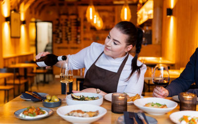 Head chef pouring a glass of wine at a table with lots of food.
