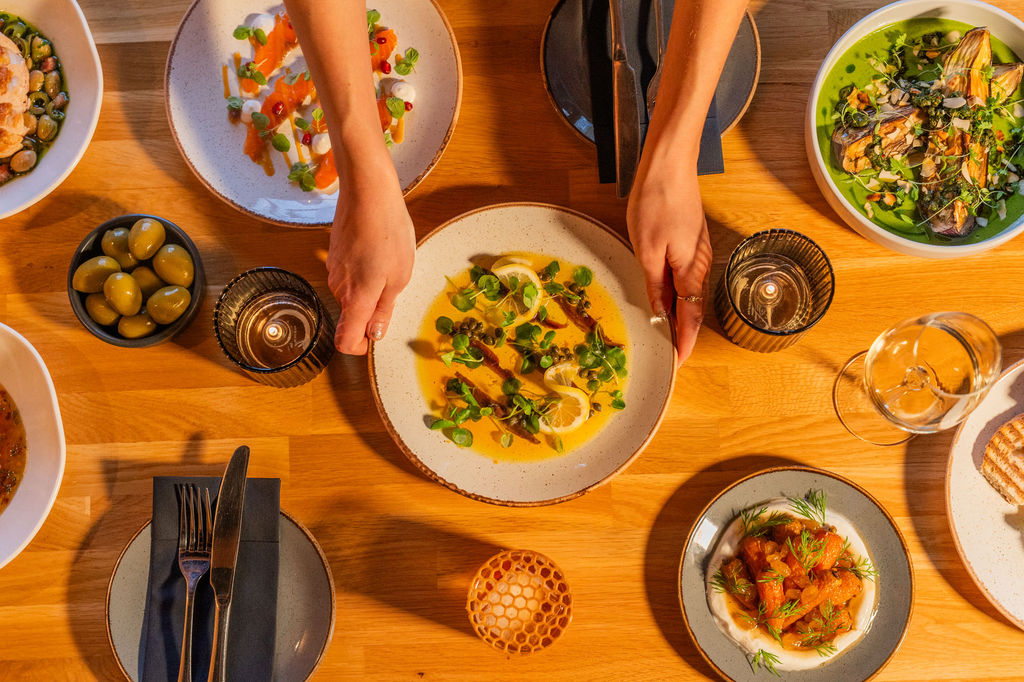Overhead photo of plates of food laid out on a table and a pair of hands placing one of the plates down.
