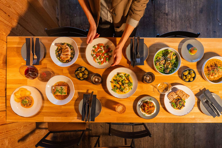 Overhead wide photo of a table with lots of different dishes of food all laid out and a man placing the final dish down.