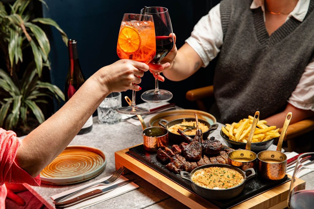 couple enjoying steak platter for two with glasses of cocktails at Kindling Brighton