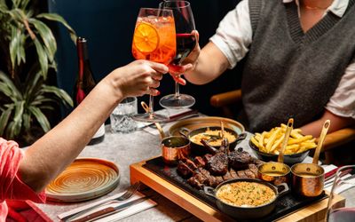 couple enjoying steak platter for two with glasses of cocktails at Kindling Brighton