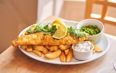 Classic fish and chips served with mushy peas, tartar sauce, and lemon wedge on a white plate.