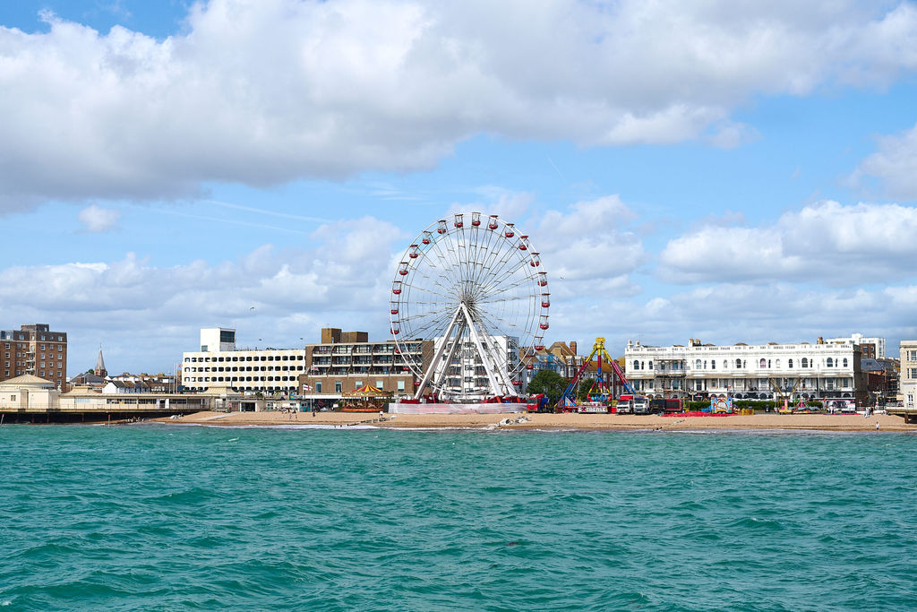 A view from the pier of the coast line of Worthing's town with the fairground and ferris wheel on the beach. Lots of places for Sussex pub walks nearby.