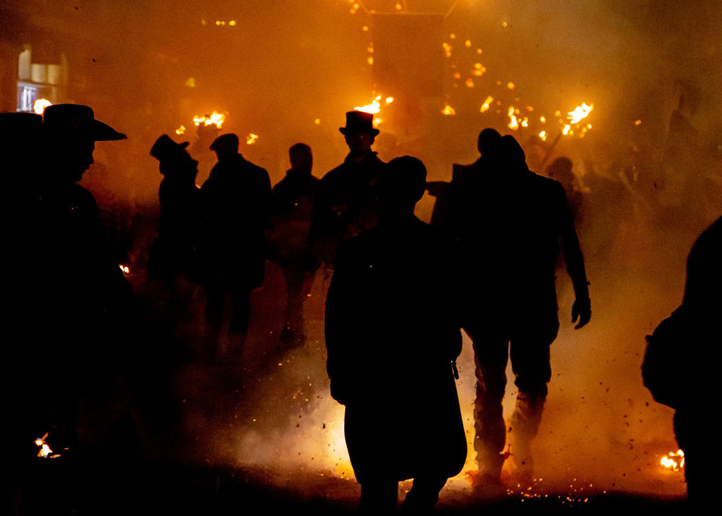 A silhouette of people at night walking along a bonfire parade with fire in the background.