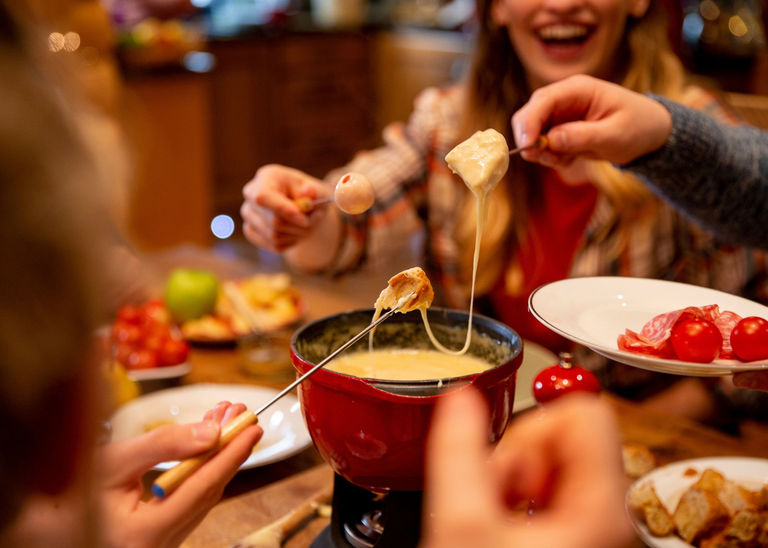 People dipping food into a cheese fondue pot and looking happy.