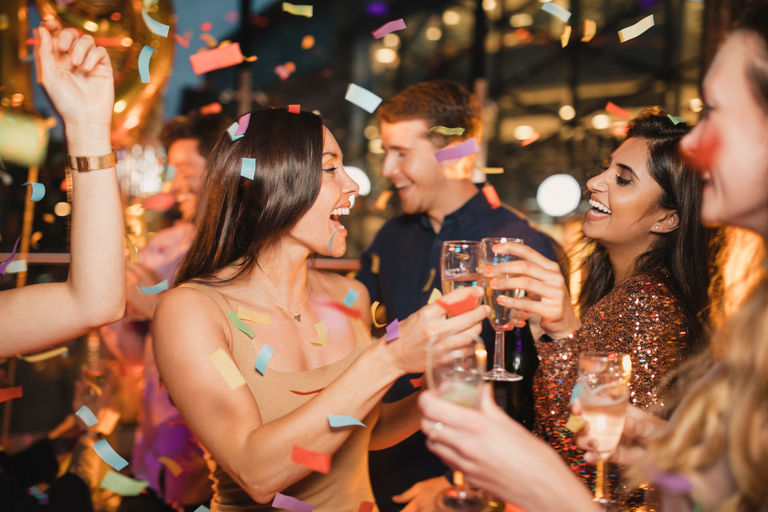 Friends dancing with confetti in the air and champagne in their hands. New Year's eve Brighton. Black Friday Brighton