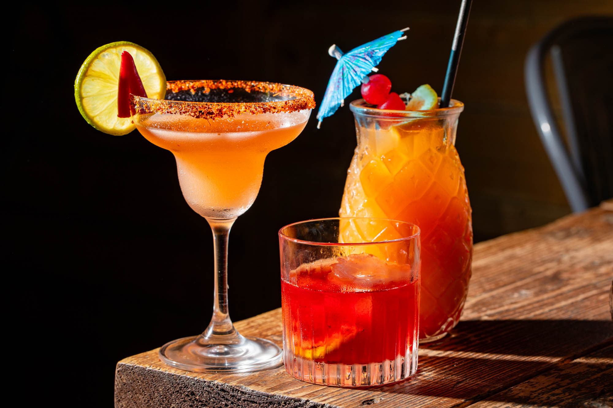 photo of three delicious orange/red cocktails served at the edge of wooden table