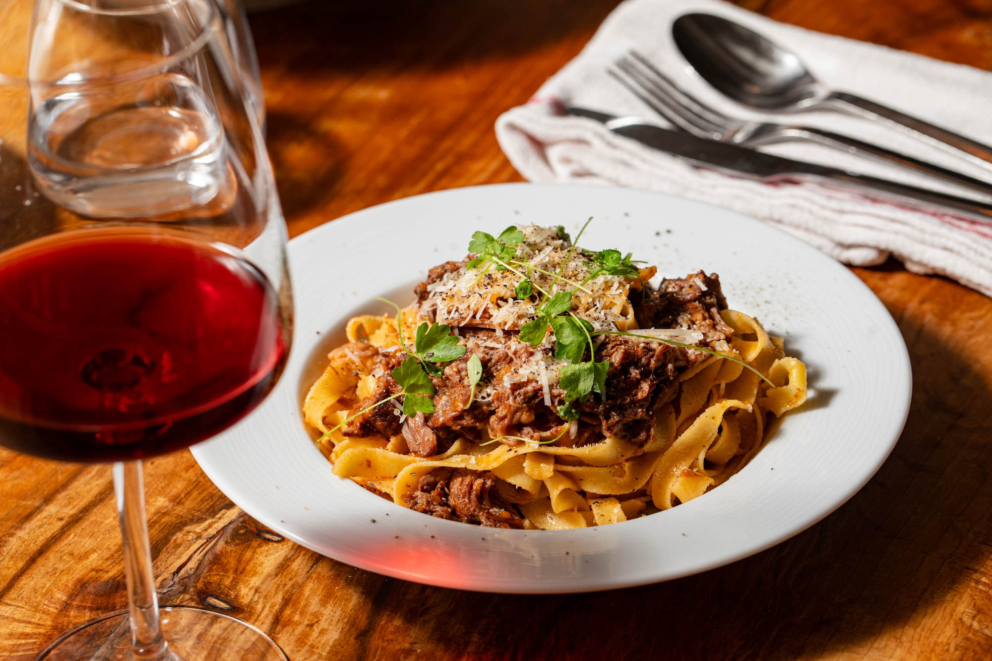 delicious pasta with parmesan, meat ad some veggies served in white plate and with glass of red wine at Poco Alfriston
