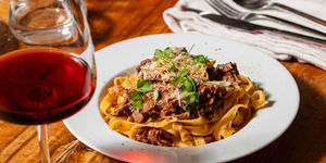delicious pasta with parmesan, meat ad some veggies served in white plate and with glass of red wine at Poco Alfriston