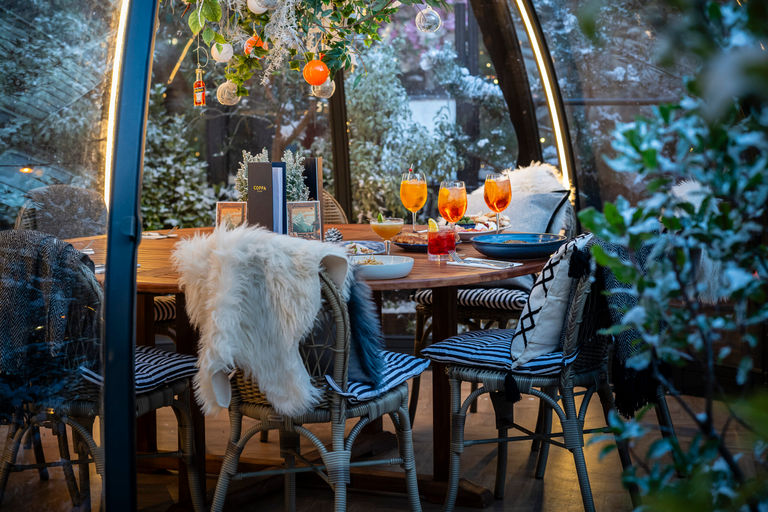 A winter igloo at Christmas with a table and chairs and blankets, snow and hanging baubles.