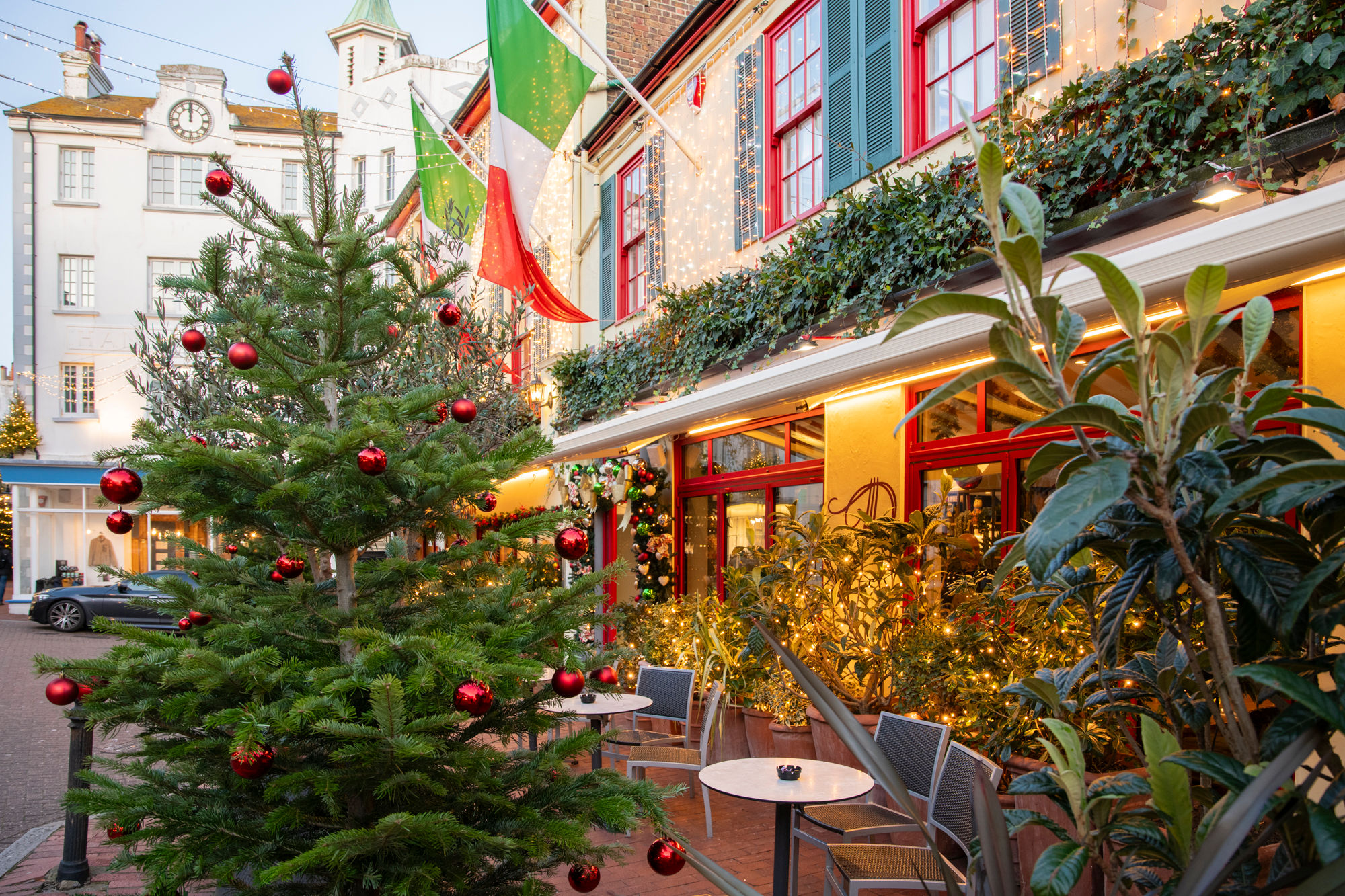 A Christmas tree outside of an Italian restaurant with Italian flags and fairy lights on the building.