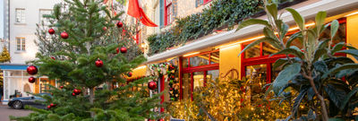 A Christmas tree outside of an Italian restaurant with Italian flags and fairy lights on the building.