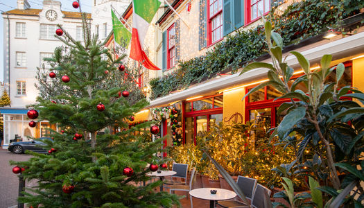 A Christmas tree outside of an Italian restaurant with Italian flags and fairy lights on the building.