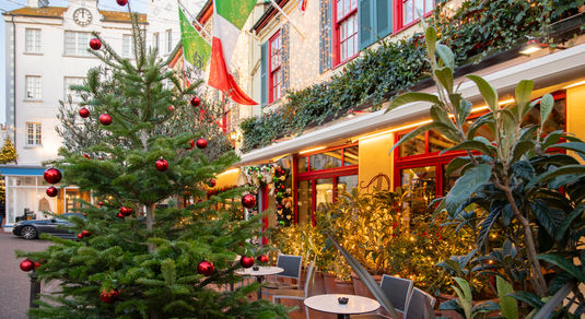 A Christmas tree outside of an Italian restaurant with Italian flags and fairy lights on the building.