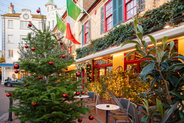 A Christmas tree outside of an Italian restaurant with Italian flags and fairy lights on the building.