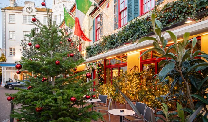 A Christmas tree outside of an Italian restaurant with Italian flags and fairy lights on the building.