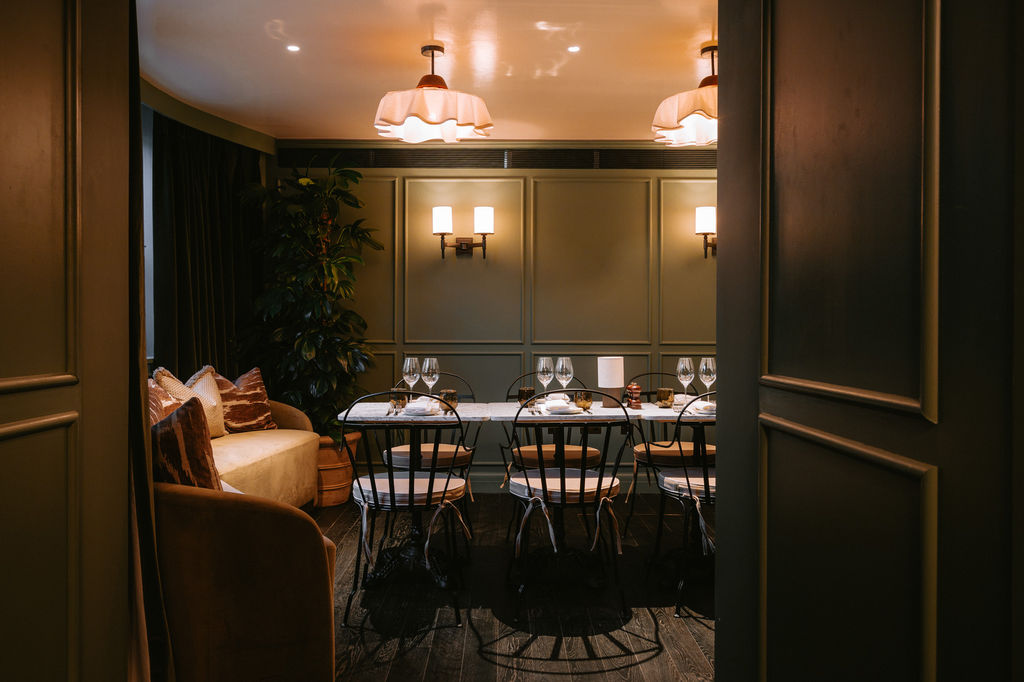 A Dining room is photgraphed through a set of doors. The table is laid and to the side there is a sofa for comfort. The walls are green and the space looks inviting.