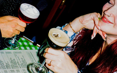 Two people celebrating with cocktails in tall glasses at Dishoom. Runner up for best cocktails in the 2026 BRAVO Awards. Public voted with 72,000 votes.