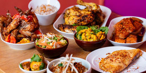 A variety of Asian dishes displayed on a wooden table with a bright pink wall behind.