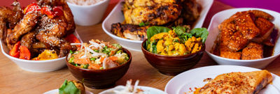 A variety of Asian dishes displayed on a wooden table with a bright pink wall behind.