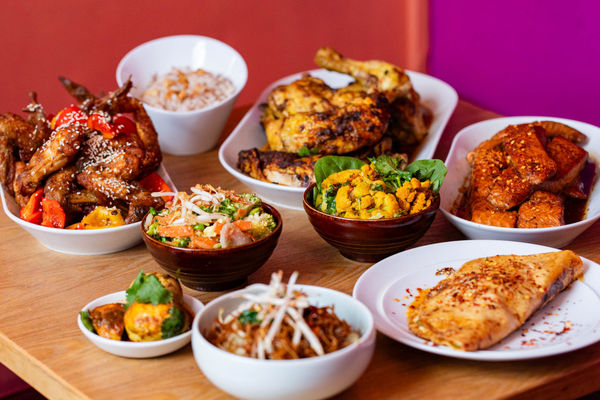 A variety of Asian dishes displayed on a wooden table with a bright pink wall behind.