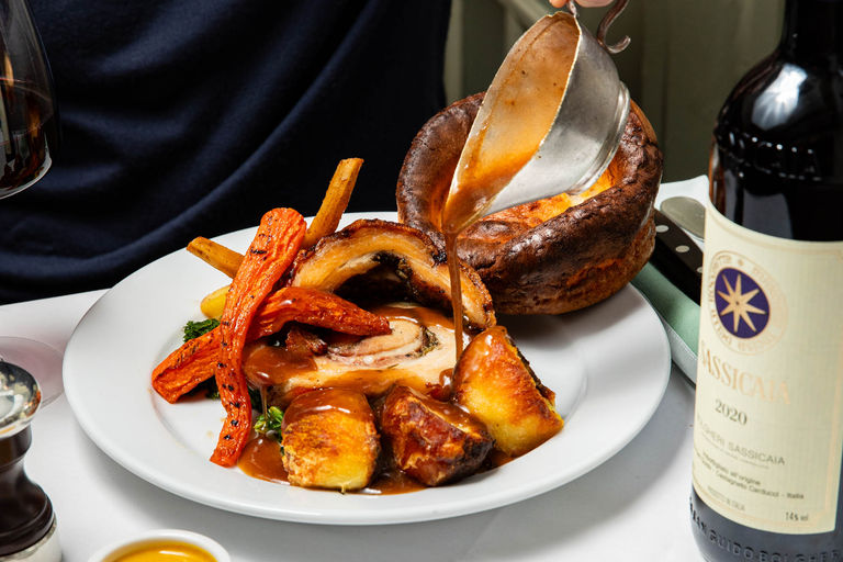 person pouring a gravy over delicious looking Yorkshire pudding served with veggies and meat at IL Bistro