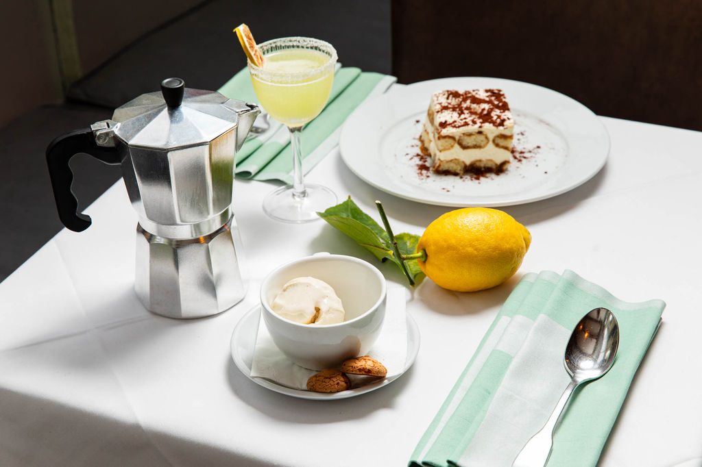 A beautifully arranged Italian dessert spread at Il Bistro, featuring classic tiramisu, affogato with amaretti biscuits, and a zesty limoncello cocktail. A traditional moka pot and a fresh lemon complete the scene, capturing the essence of an authentic Italian dining experience.