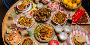 A vegan feast of food and dishes all laid out with drinks and ingredients on a large wooden table.