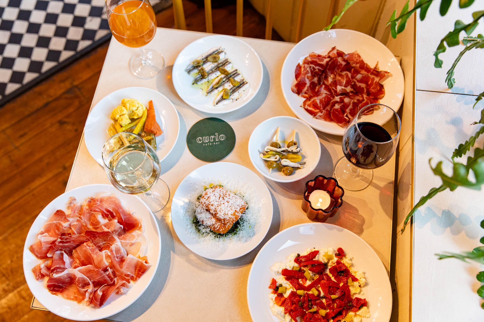over head shot of the square white table at Curio, laid out with 7 small plates and drinks.
