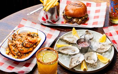 side shot of the wooden table with burger and fries, oysters, shrimps and cocktails at Boysterous Burgers