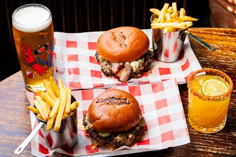 two incredible looking burgers with fries and drinks at the Fountain Head Pub. Boysterous Burgers are new to the Brighton pub scene. On a chequered red and white table cloth.